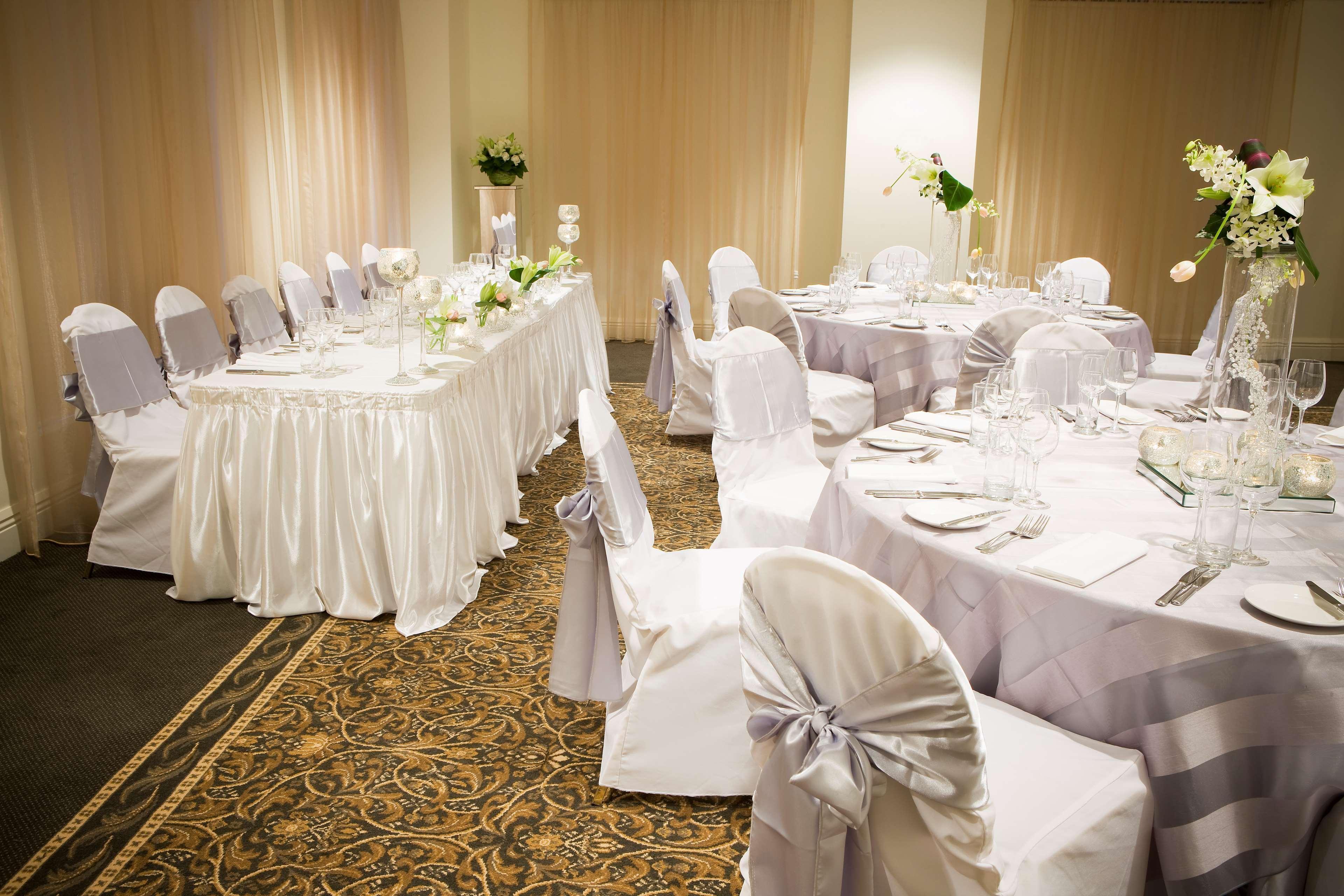 Stamford Plaza Melbourne Hotell Exteriör bild The photo depicts an elegantly set dining area, likely for a special event or celebration. There are several round tables covered with tablecloths, each set with plates, glassware, and cutlery. The chairs are dressed in white covers, some adorned wit