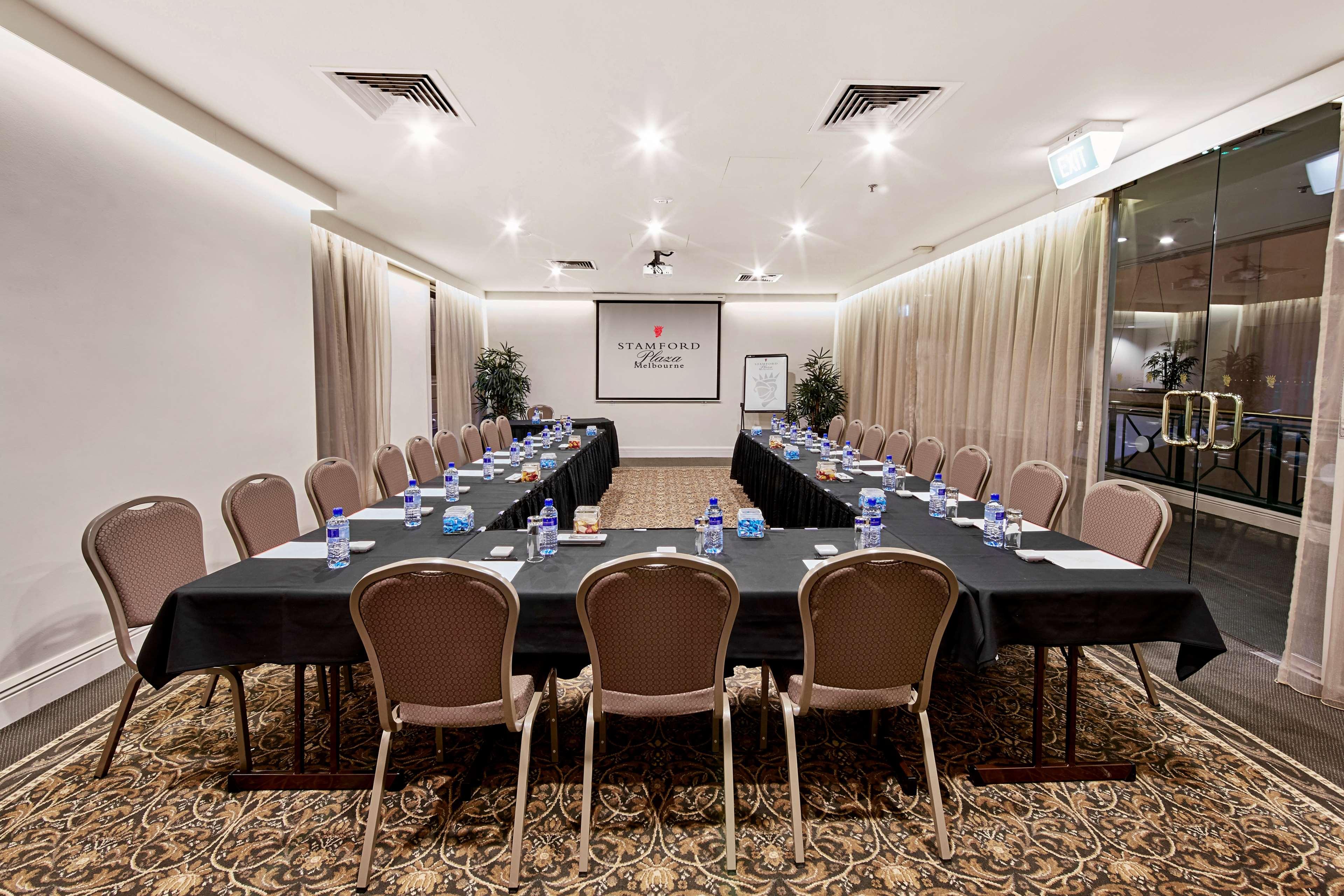 Stamford Plaza Melbourne Hotell Exteriör bild The photo shows a conference room set up for a meeting. There are several long tables arranged in a U-shape, covered with black tablecloths. Each table has a water bottle and notepad placed at intervals. The room is well-lit, with light-colored walls