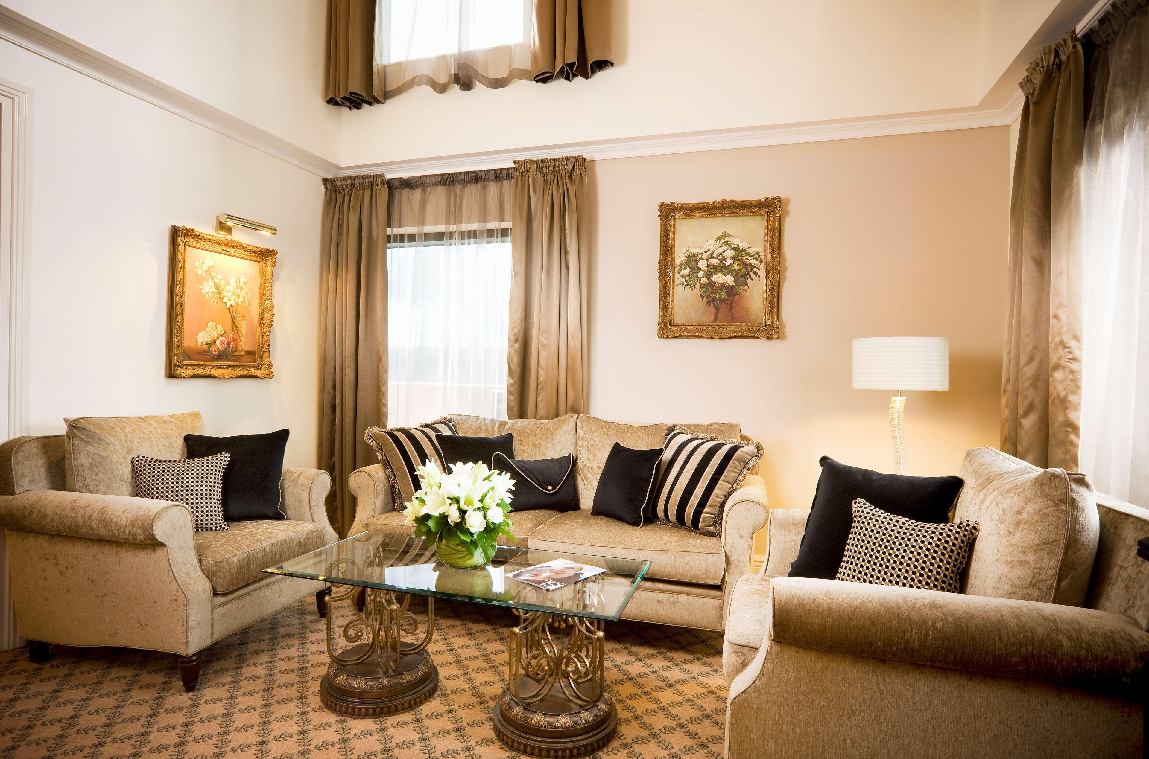 Stamford Plaza Melbourne Hotell Rum bild The photo depicts a stylish living room with a warm and inviting aesthetic. It features a set of comfortable beige sofas adorned with decorative pillows in black and patterned designs. There is a glass coffee table at the center, supported by elegant