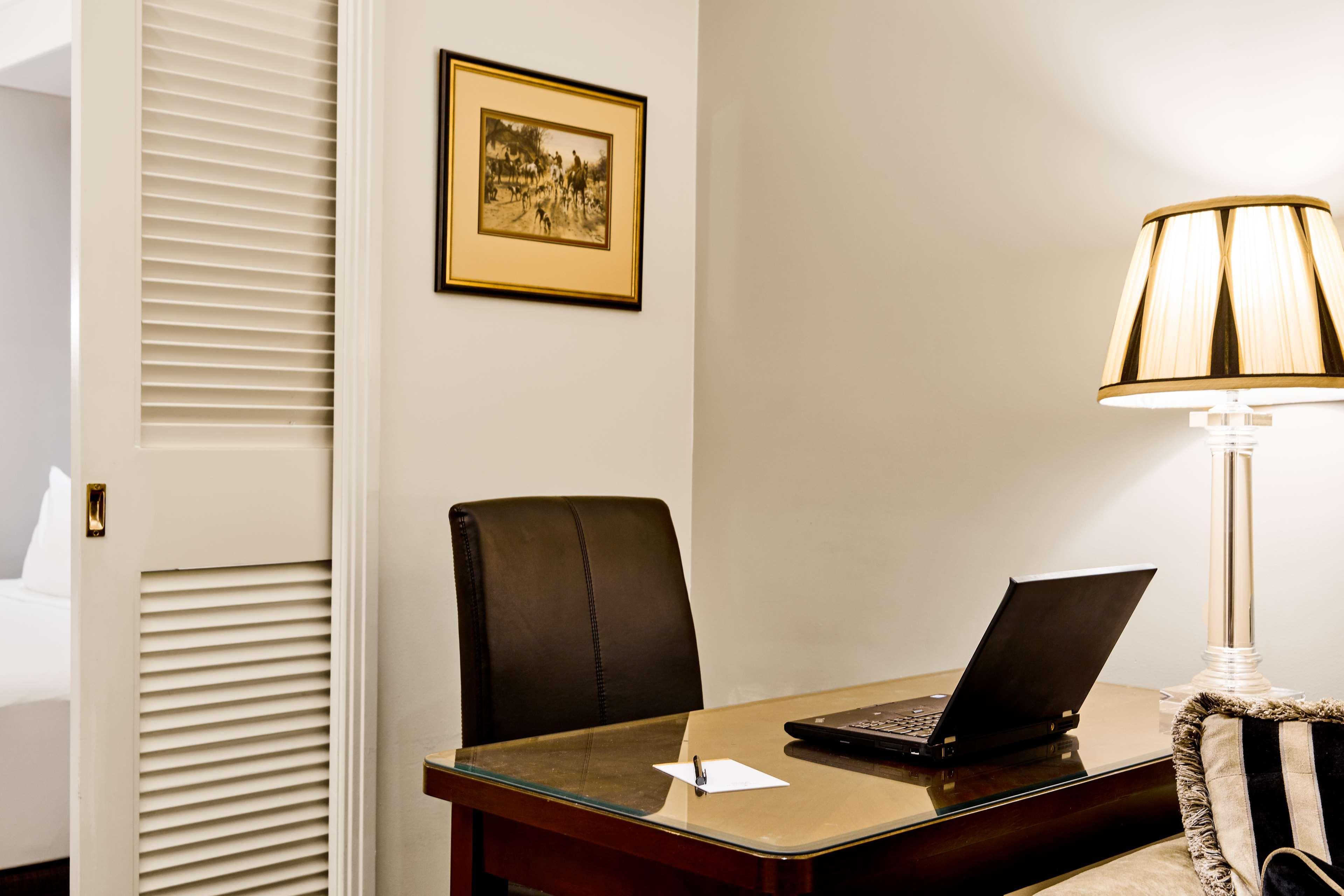 Stamford Plaza Melbourne Hotell Exteriör bild The photo shows a small office or workspace. There is a desk with a glass surface, and on it sits a laptop computer. A piece of paper or notecard is also placed on the desk. Behind the desk is a black office chair. A wall lamp with a striped shade is