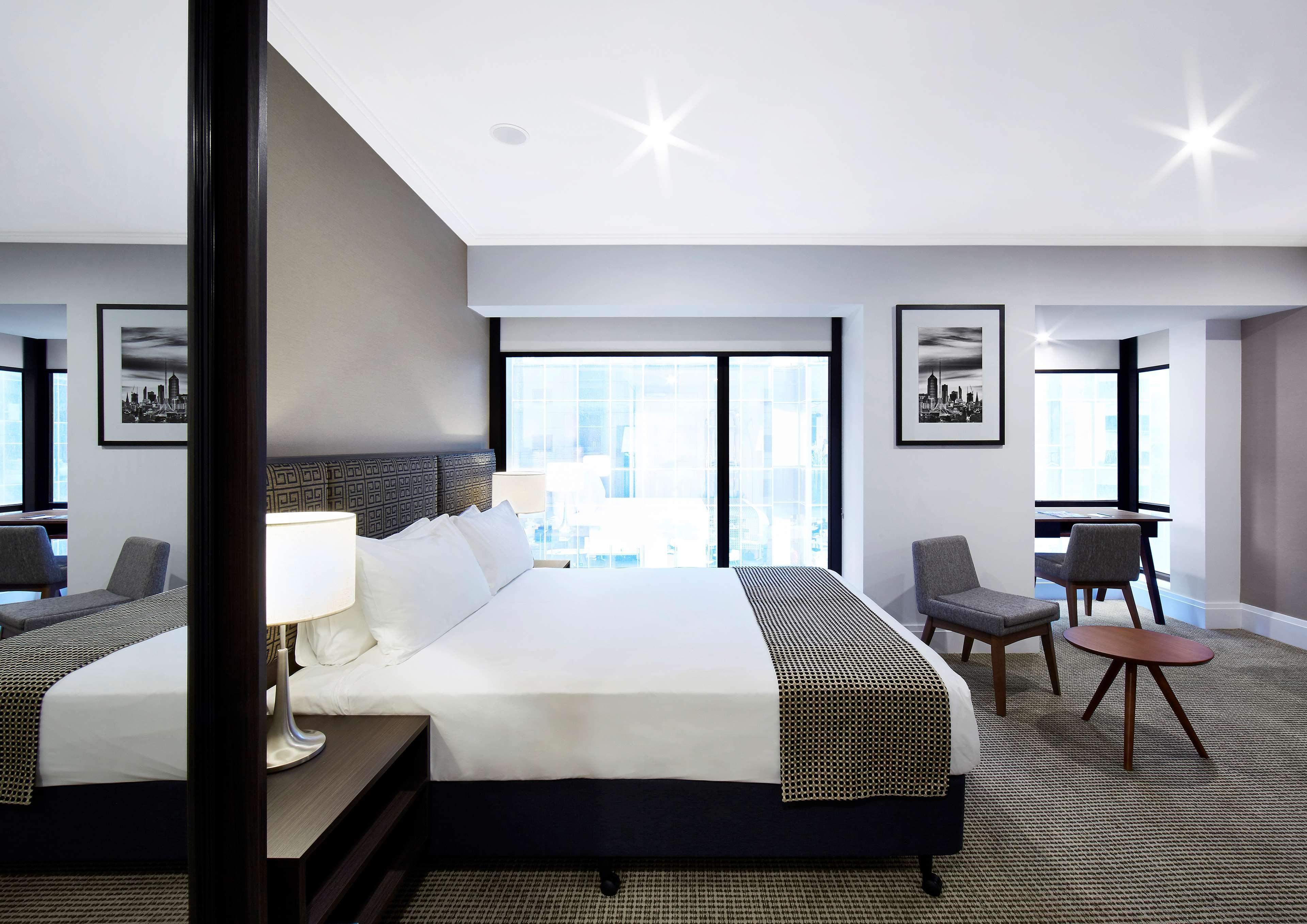 Stamford Plaza Melbourne Hotell Exteriör bild The image shows a modern hotel room featuring a large bed with white linens and a gray throw blanket. There are two windows that allow natural light to enter the space, and the walls are painted in a light color. In addition to the bed, there are two