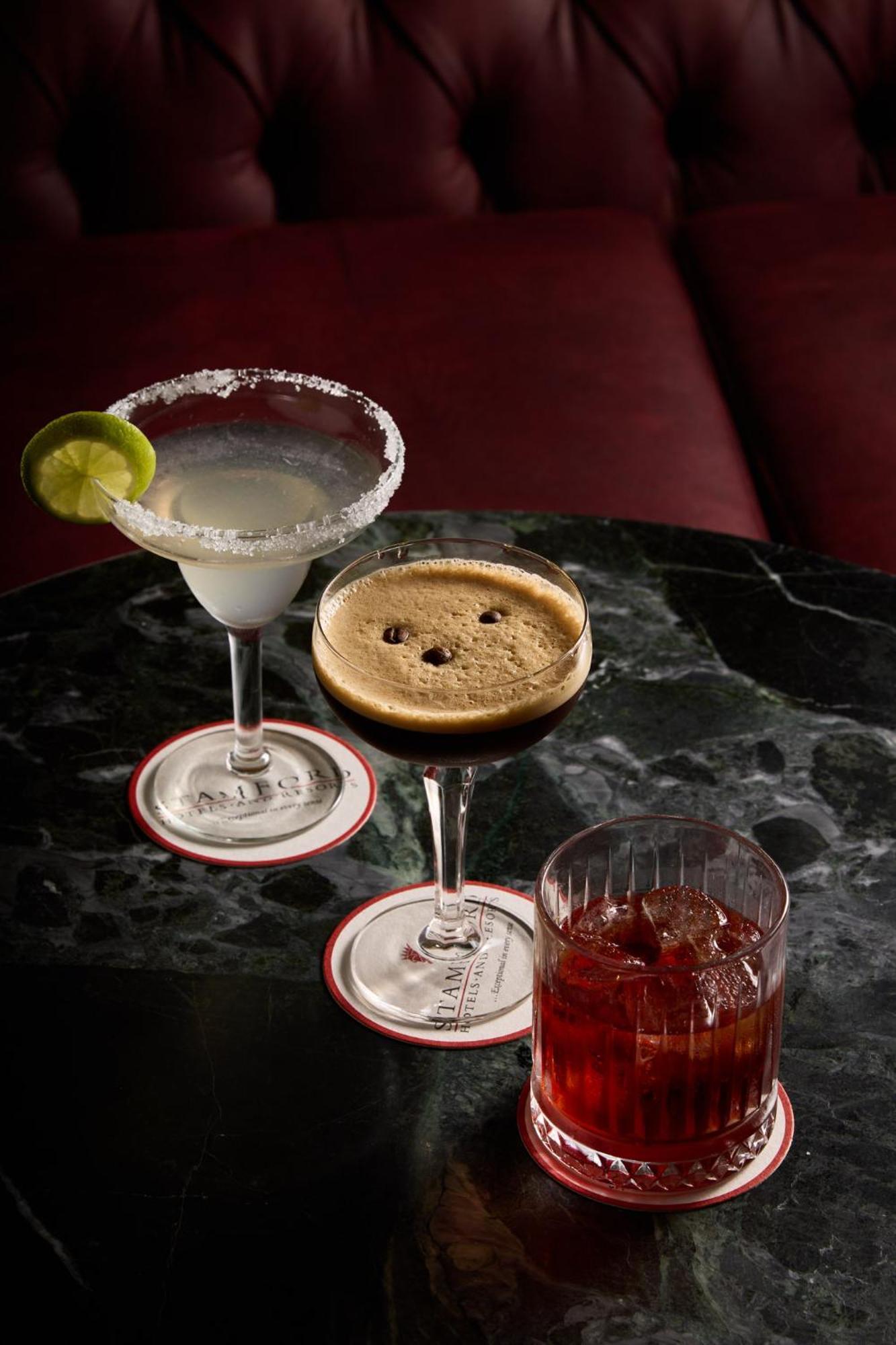 Stamford Plaza Melbourne Hotell Exteriör bild The photo displays three different cocktails arranged on a dark marble table. 

1. On the left, there is a margarita glass filled with a clear drink, garnished with a lime slice and featuring a salted rim.
2. In the center, a coupe glass holds a dark
