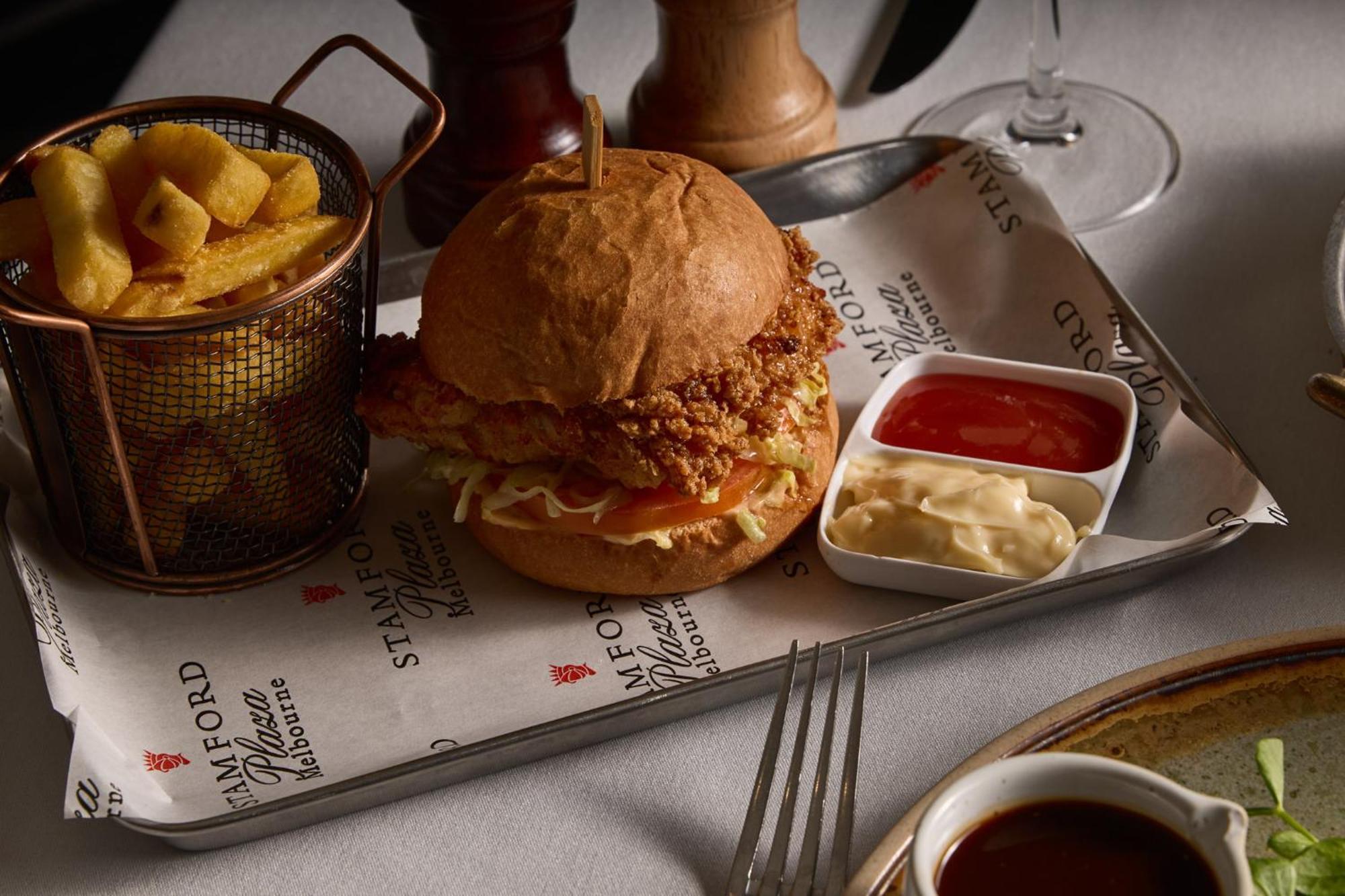 Stamford Plaza Melbourne Hotell Exteriör bild The photo features a meal served on a tray. In the center is a sandwich made with a golden-brown chicken fillet that appears crispy, placed inside a soft bun. The sandwich is likely complemented by some type of sauce or condiments underneath the chic