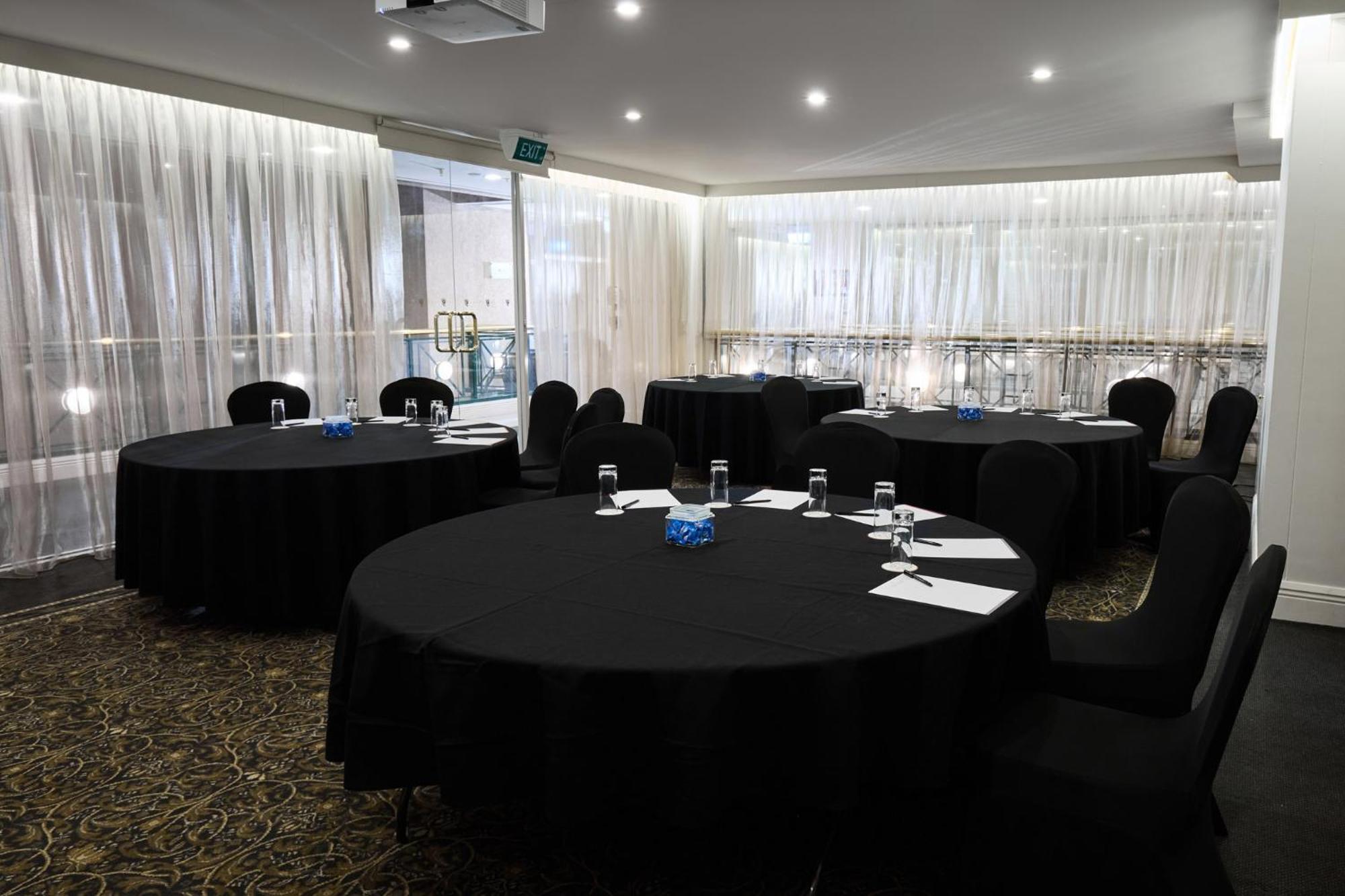 Stamford Plaza Melbourne Hotell Exteriör bild The photo shows a meeting or conference room set up with several round tables covered in black tablecloths. Each table is accompanied by black chairs. There are some white notepads and pens placed on the tables, and a small decorative item, possibly 