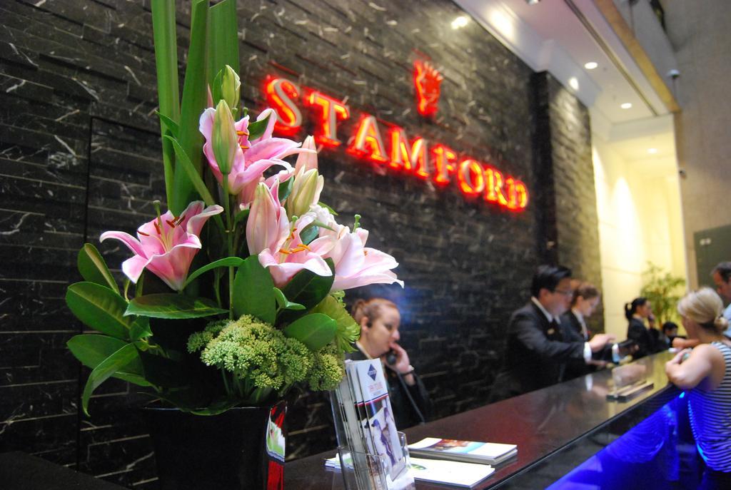 Stamford Plaza Melbourne Hotell Exteriör bild The photo shows a hotel reception area with a prominent sign that reads "STAMFORD" in bright red letters. In the foreground, there is a decorative arrangement of flowers, primarily featuring pink lilies, along with greenery. The reception counter is 